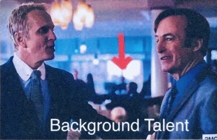 Foreground: busts of 2 major characters talking face to face. Between them is a red arrow pointing to a fuzzy image of a person in the background, features indistinguishable.